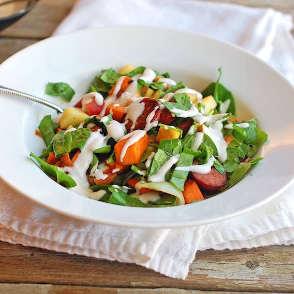 Harvest salad with sweet potato, spinach, turkey kielbasa, bacon, apples, and topped with a creamy homemade maple dressing.
